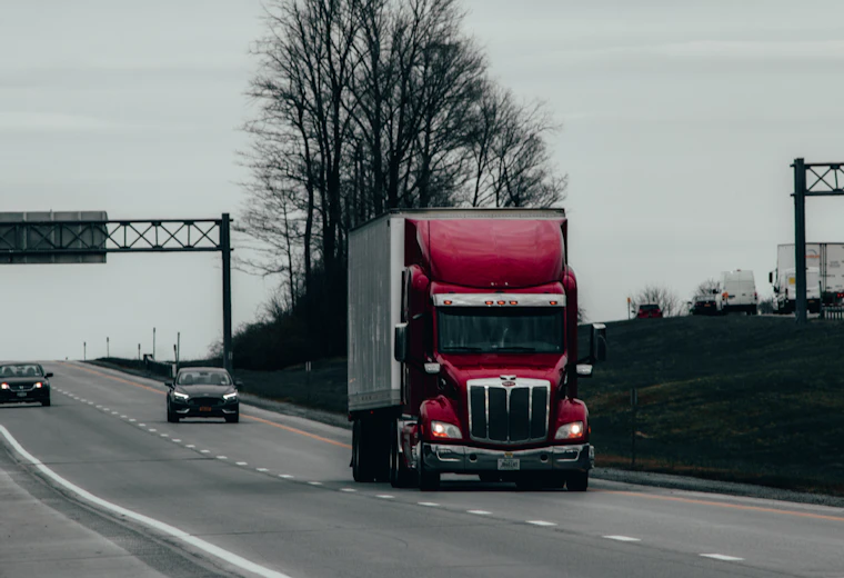 A red tractor-trailer driving on a divided highway past an overhead sign gantry