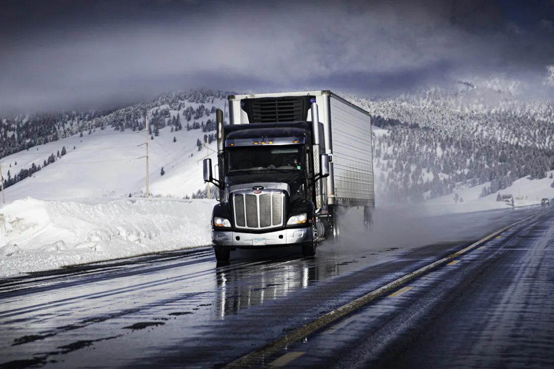 A tractor pulling a refrigerated trailer on a wet highway between snowbanks