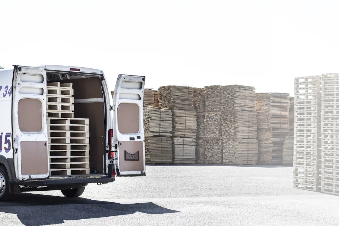 A white cargo van with its rear doors open, loaded with wooden pallets